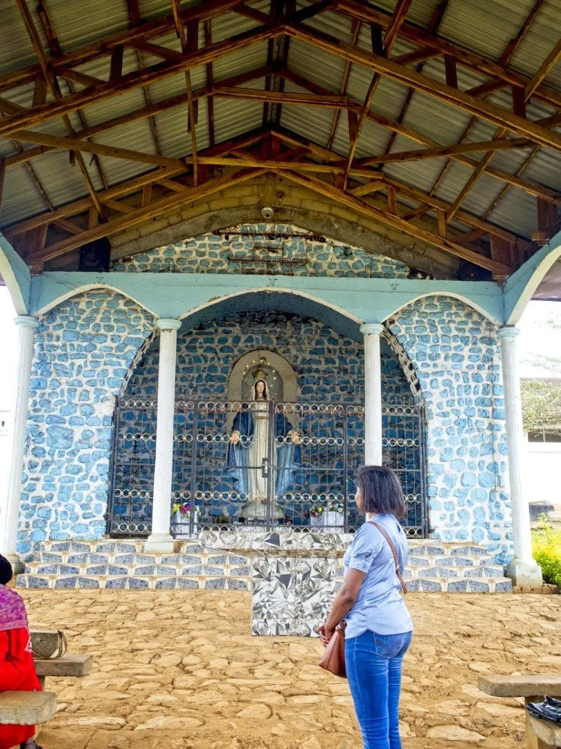Une chapelle ouverte aux murs de pierres bleutées, abritant une statue mariale