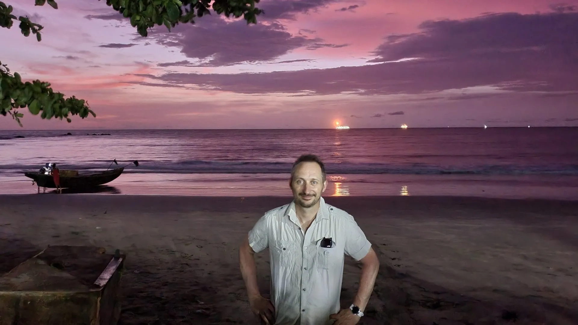 Une personne debout sur la plage devant un ciel rose et l'océan au crépuscule