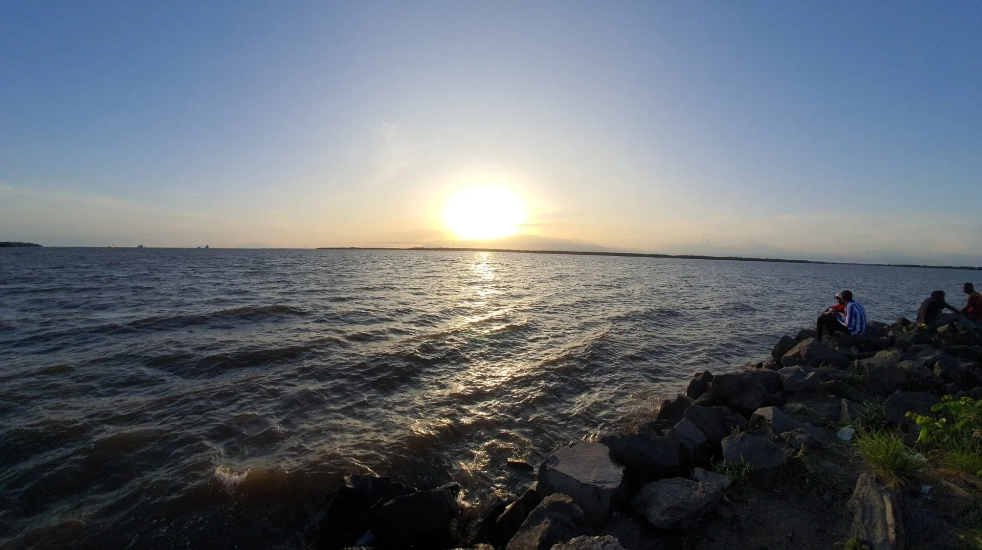 Le soleil se couchant sur l'estuaire du Wouri, des rochers sombres au premier plan