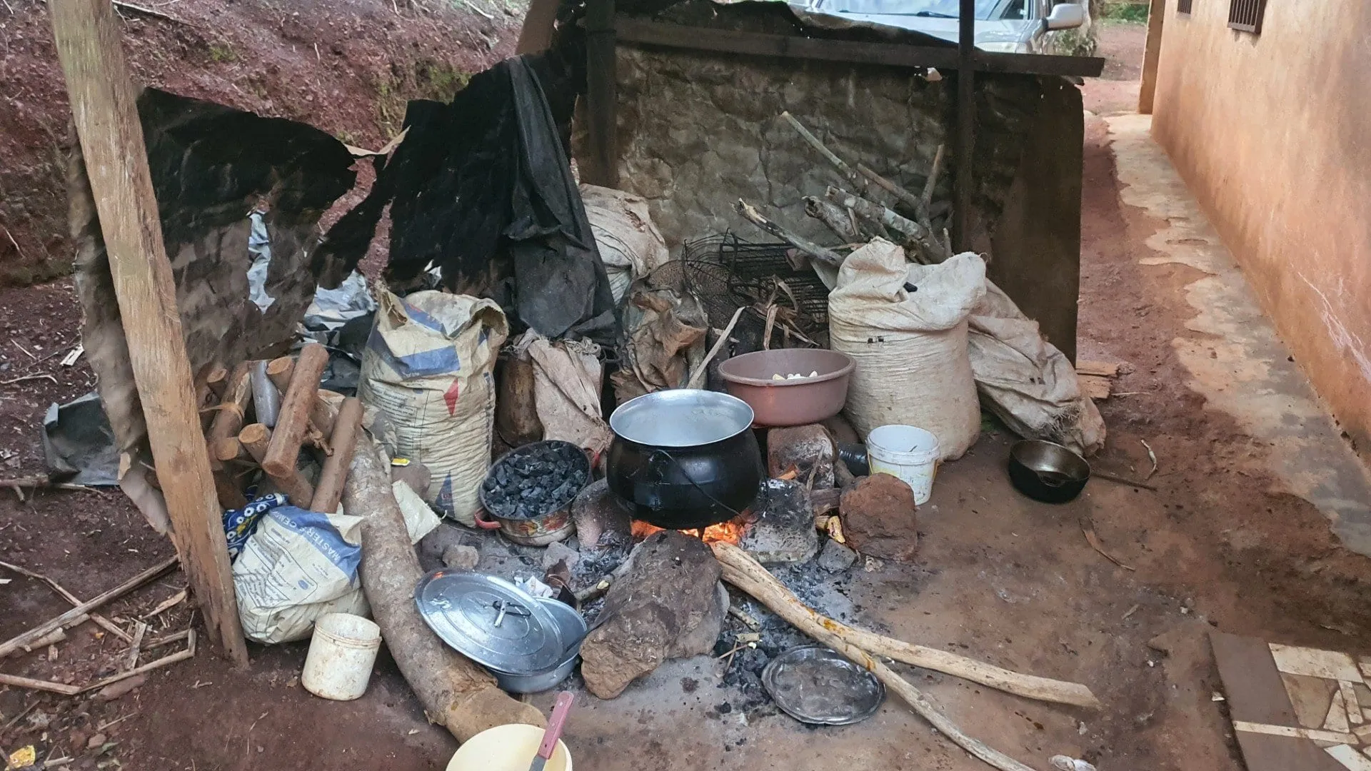 Une cuisine en terre battue, marmites posées sur un feu de bois, ustensiles au sol