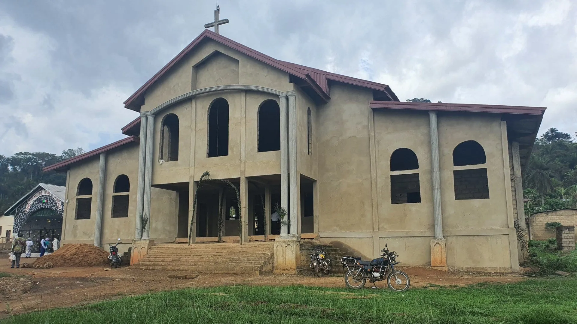 Une église ocre à toit à deux pentes surmonté d'une croix, sous un ciel nuageux