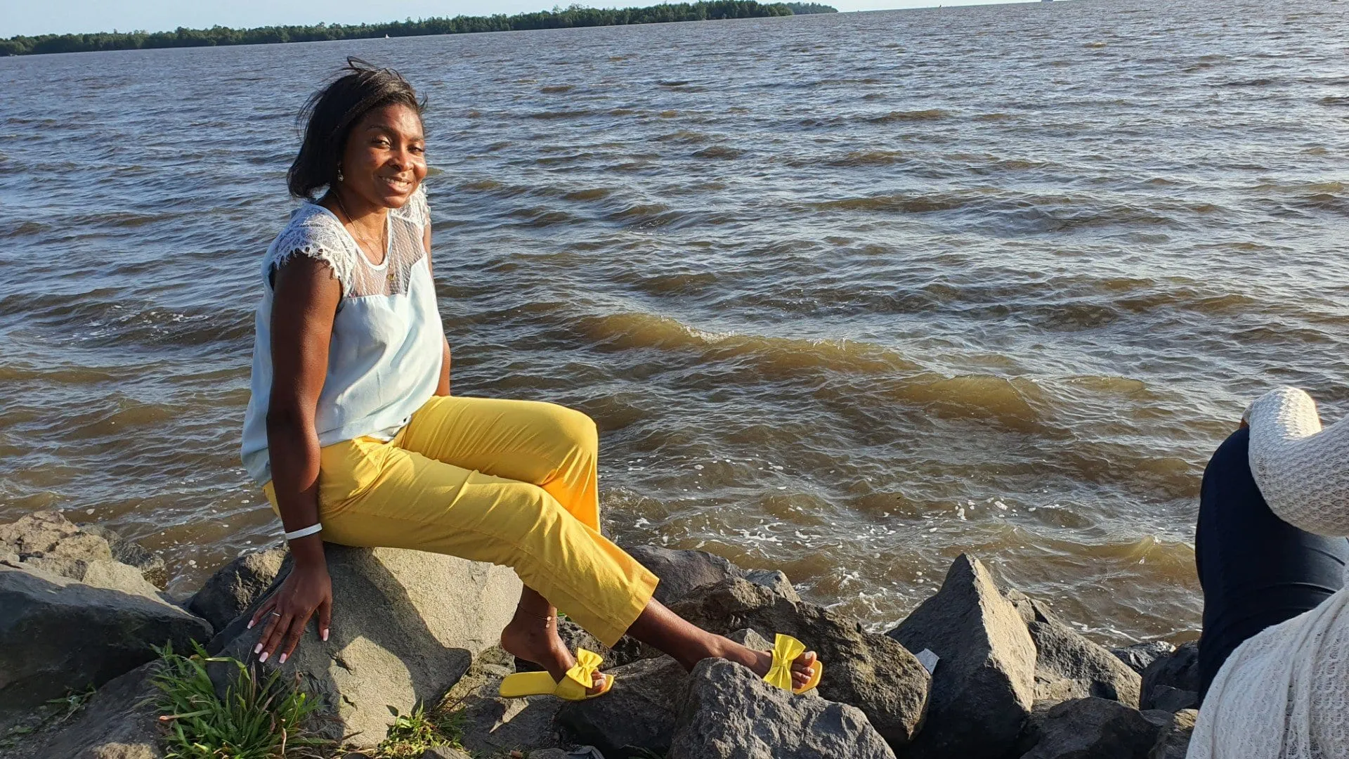 Une personne assise sur des rochers au bord de l'estuaire du Wouri, l'eau large derrière