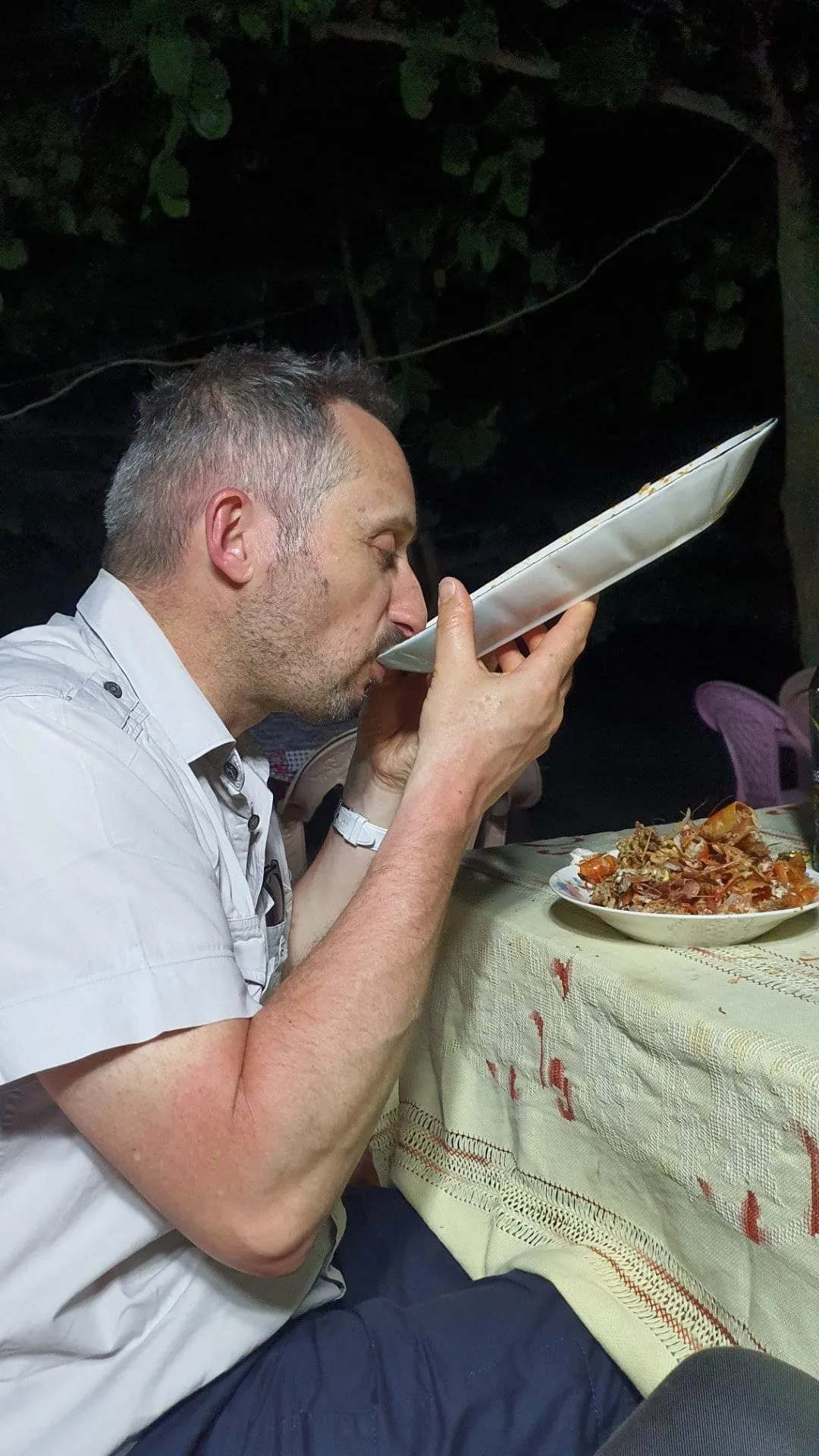 Un homme attablé tenant une grosse gambas grillée devant son assiette