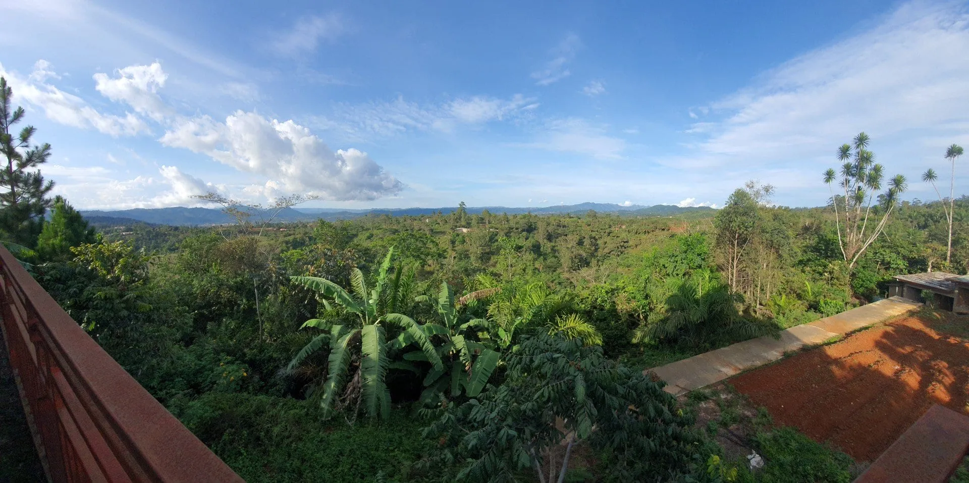 Un panorama sur des collines boisées et des toits épars, ciel nuageux