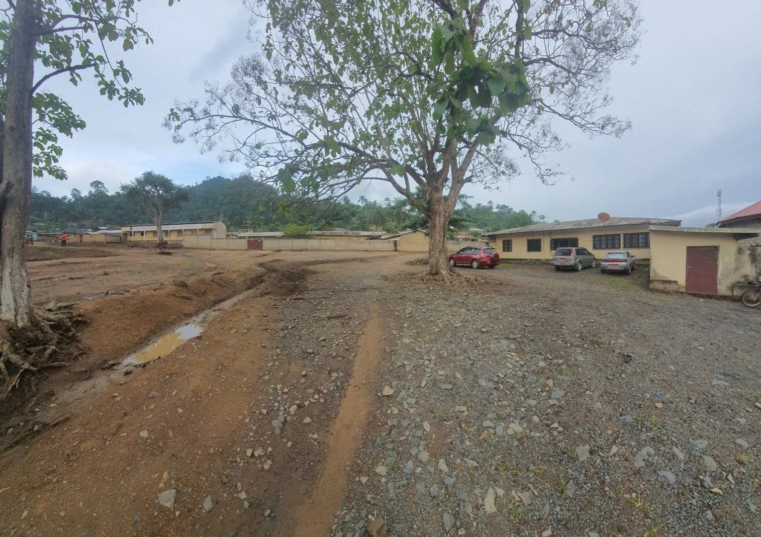 Une piste de latérite rouge bordée de maisons basses, en fin de journée