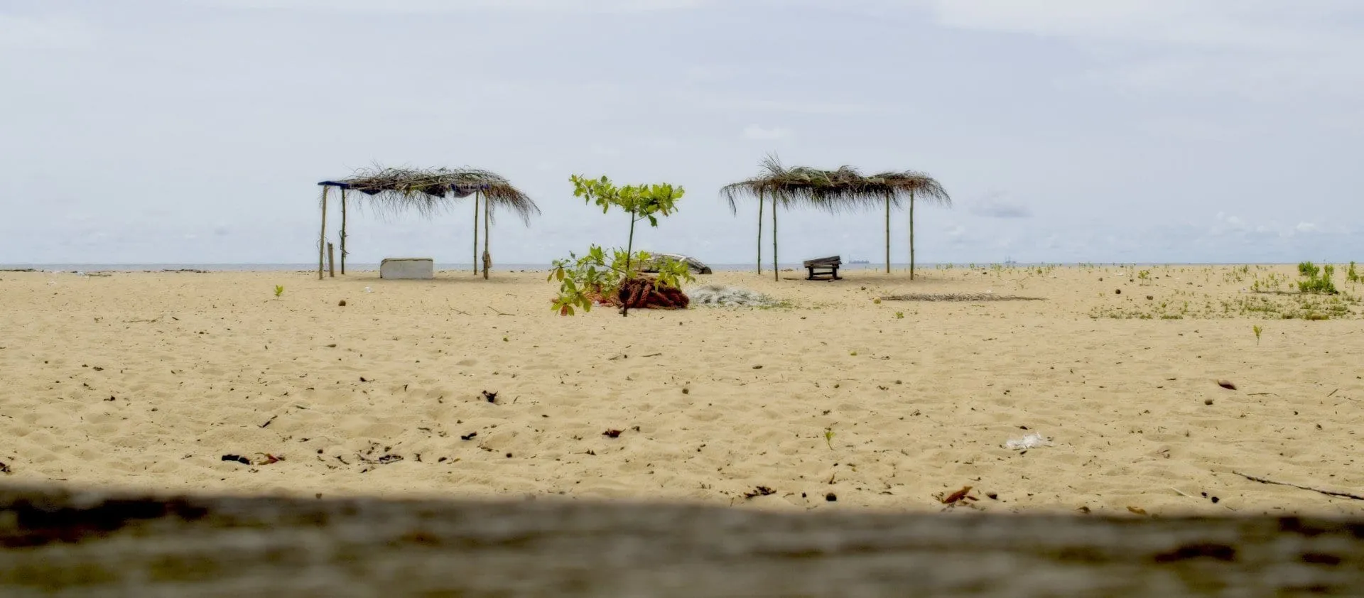 Une plage de sable clair bordée de paillotes, l'océan à gauche