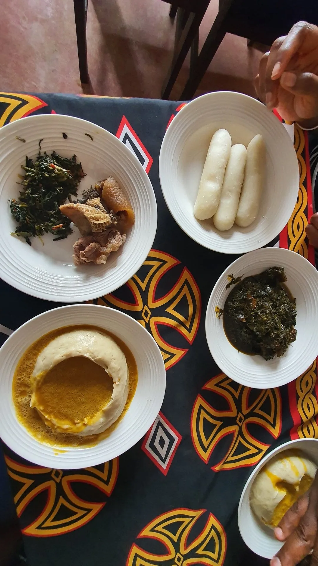Plusieurs assiettes disposées sur une nappe colorée, dont un bâton de manioc blanc et un plat en sauce verte