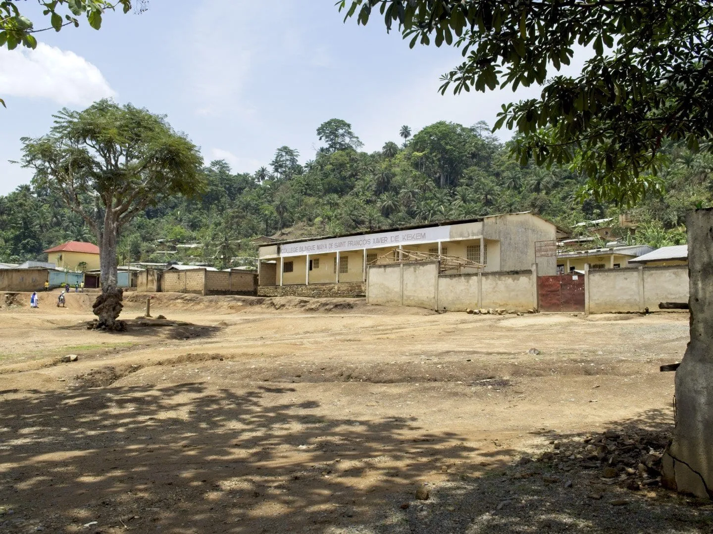 Un village aux bâtiments bas sur une terre rouge, végétation et collines derrière