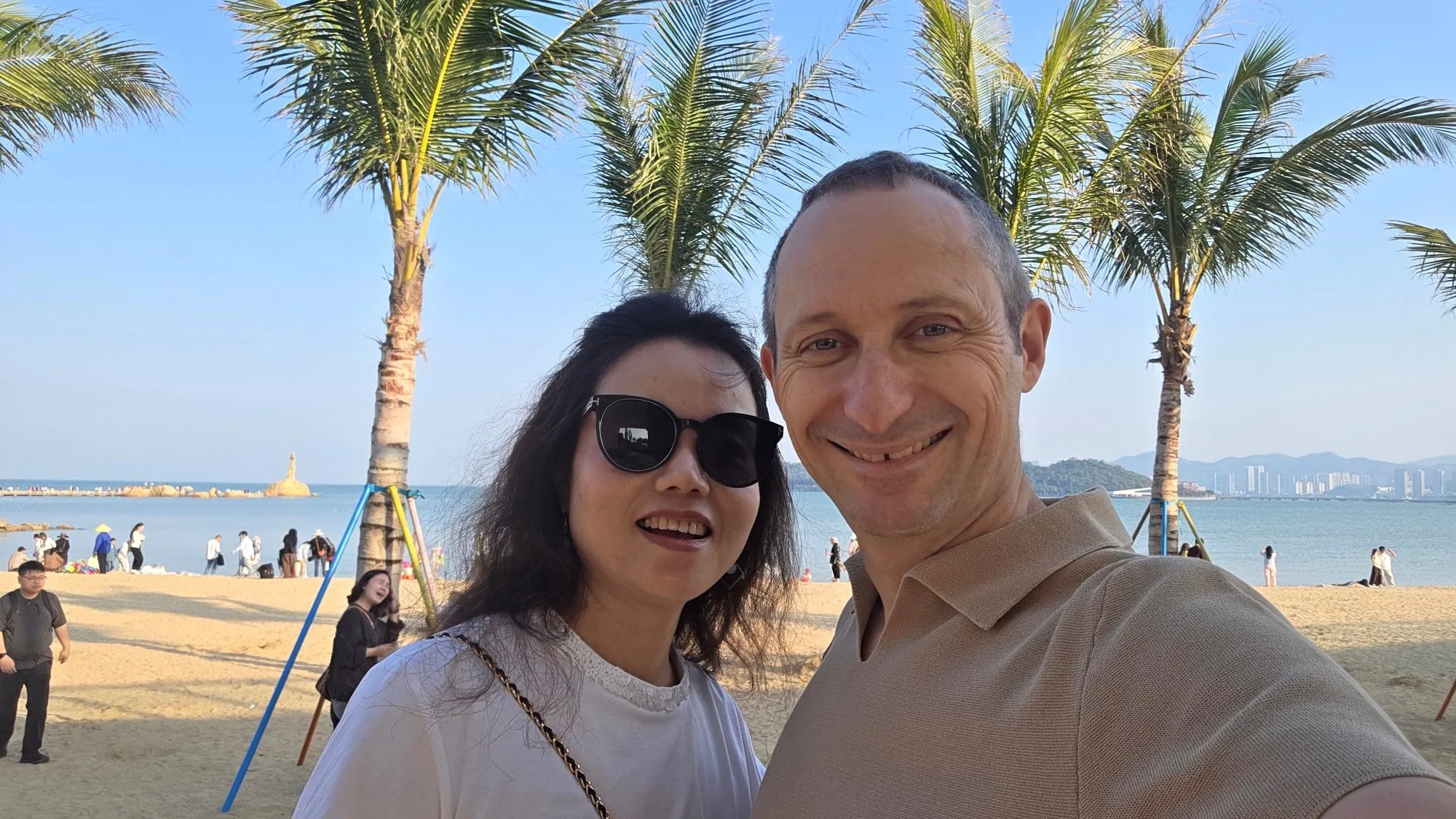 Une plage bordée de palmiers à Zhuhai, en plein jour, la mer et des reliefs au fond