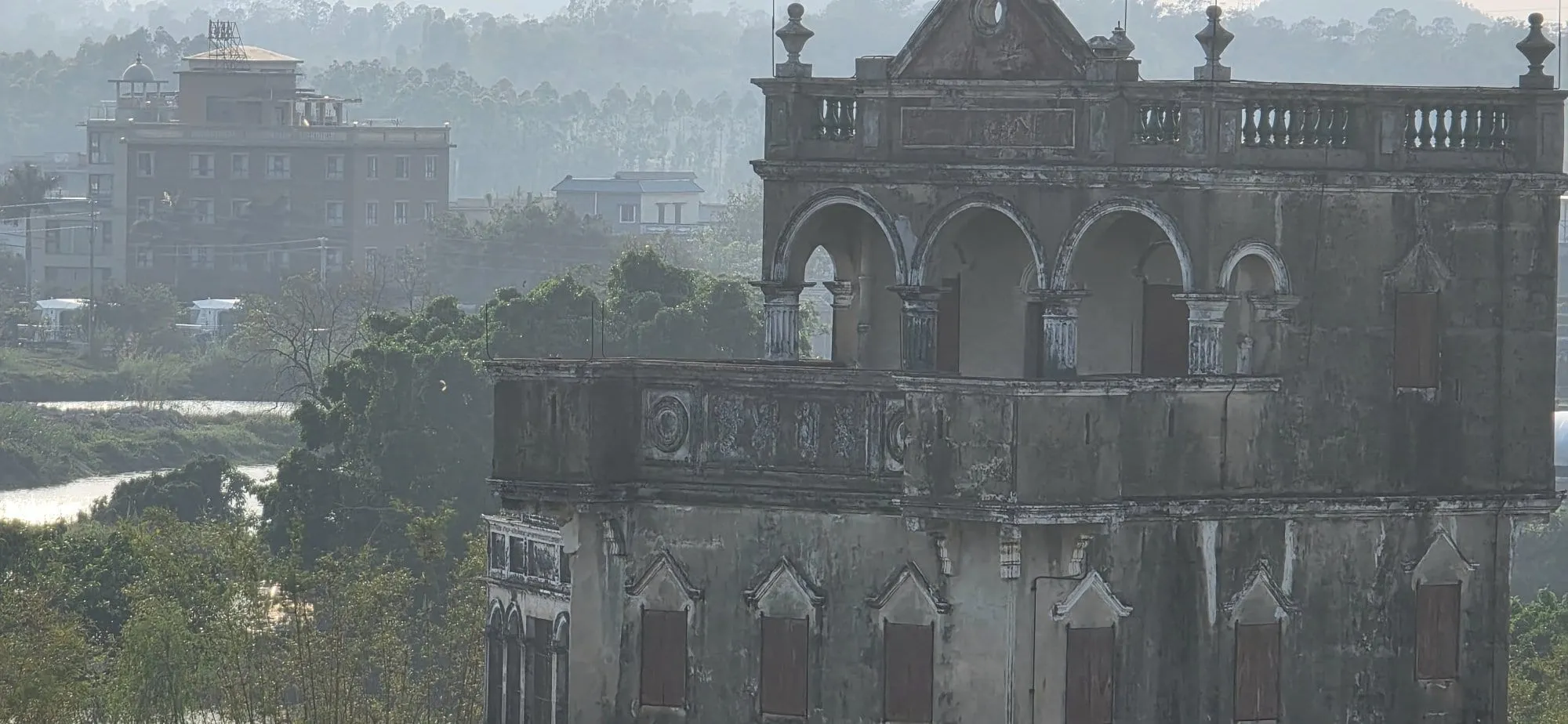 Une tour diaolou en contre-jour dans la brume, silhouette sombre sur un ciel pâle