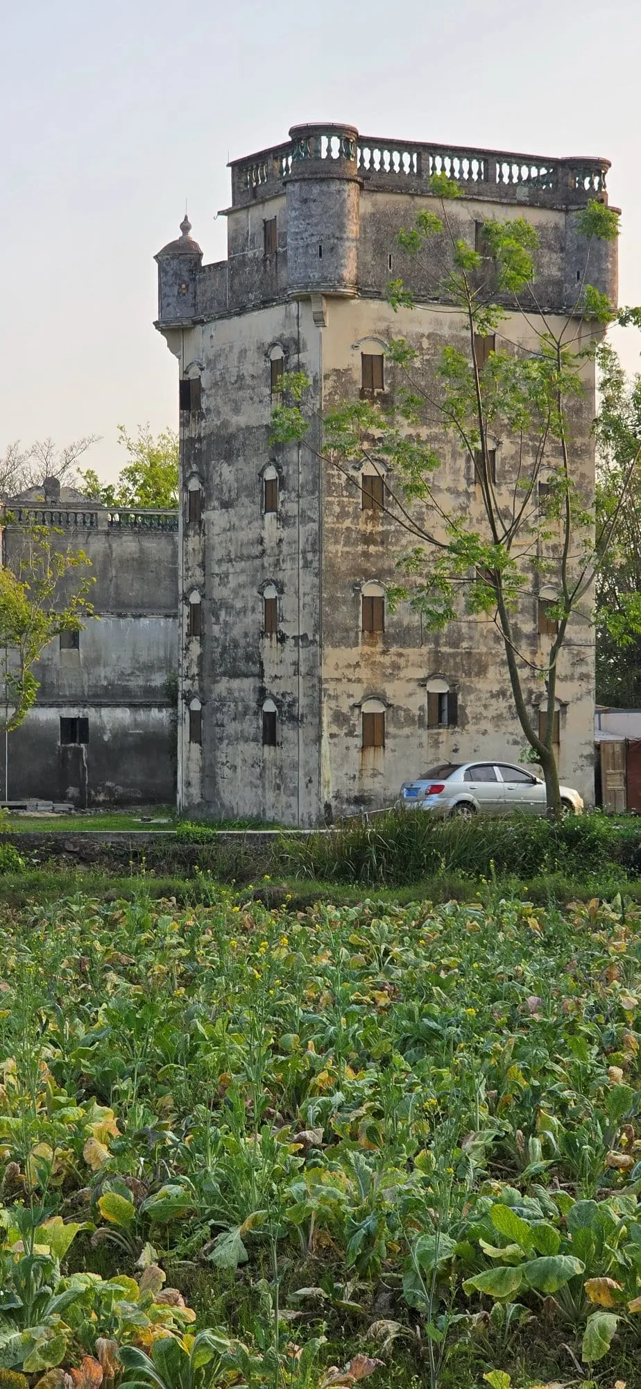 Une tour diaolou isolée en bord de champ, une voiture garée à son pied