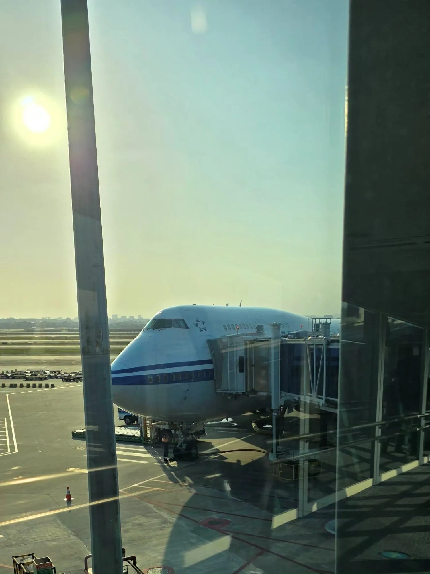 Un Boeing 747 blanc et bleu vu depuis la salle d'embarquement, à travers une baie vitrée