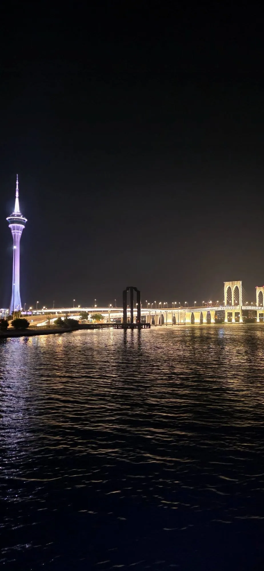 La silhouette de Macao illuminée de nuit vue depuis l'eau, une tour et un pont éclairés