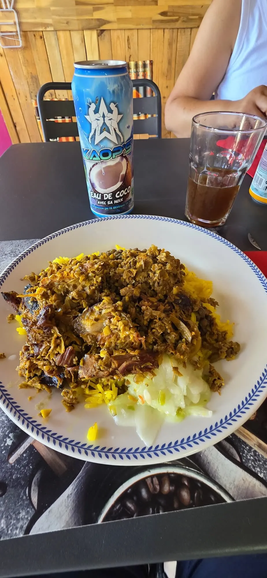 Une assiette de cari avec riz et grains, canette de boisson locale sur une table simple