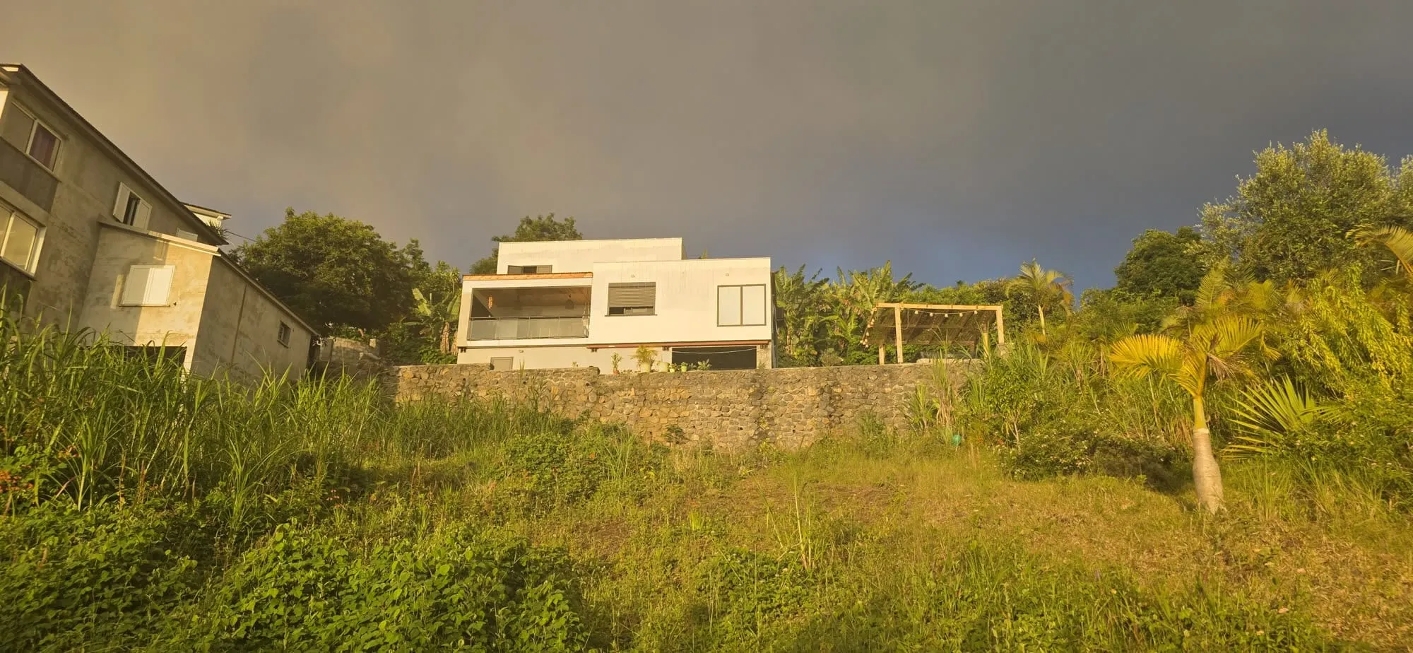 Un jardin en pente et une maison claire sous un ciel de fin de journée