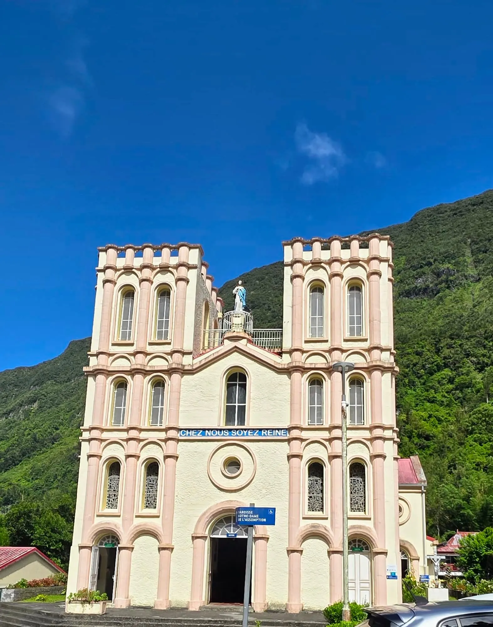La façade claire d'une église à deux clochers, montagne verte derrière