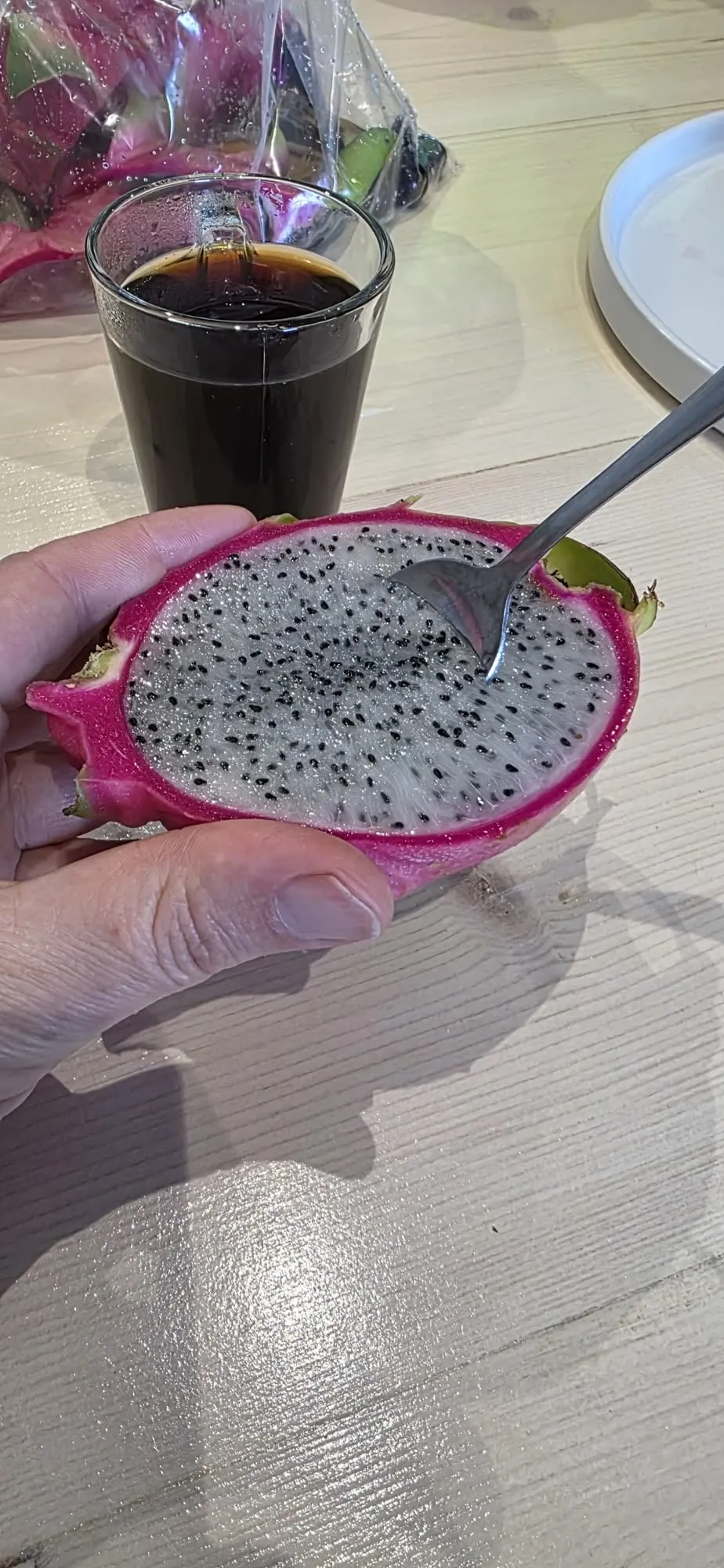Un fruit du dragon coupé en deux dans son écorce rose, cuillère et café
