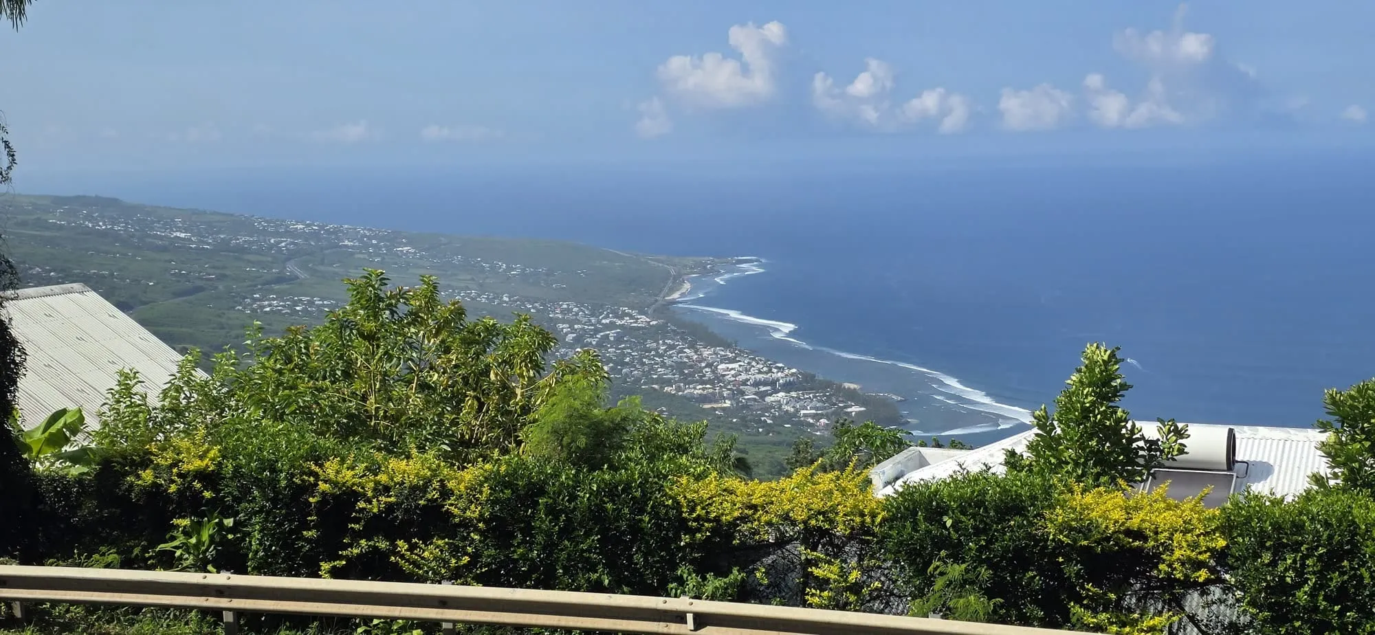 Vue plongeante sur le lagon et la barrière de corail depuis les hauteurs, végétation au premier plan
