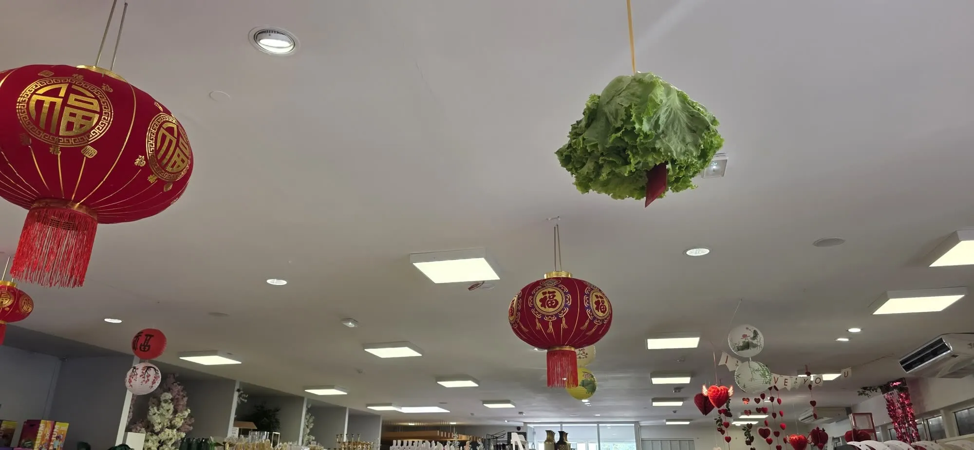 Des lanternes rouges au plafond d'une galerie, une laitue verte suspendue à un fil