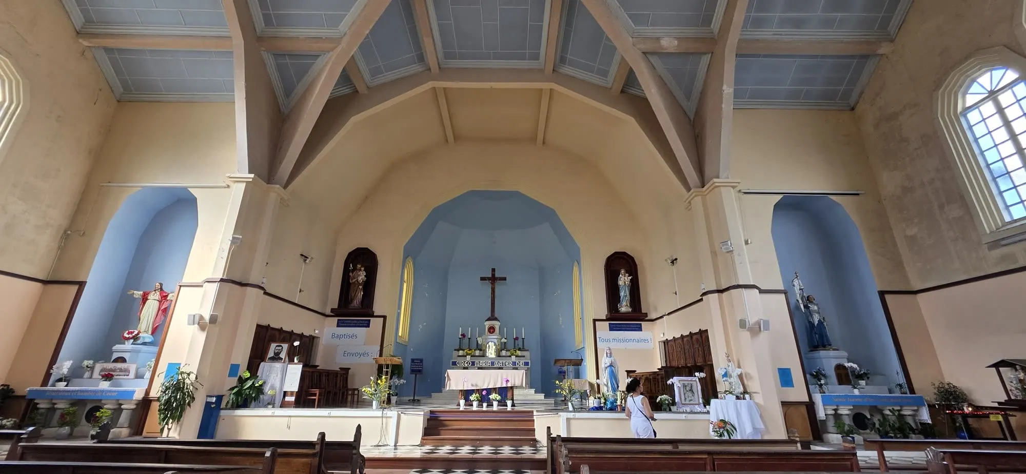 La nef claire d'une église à charpente apparente, autel fleuri au fond