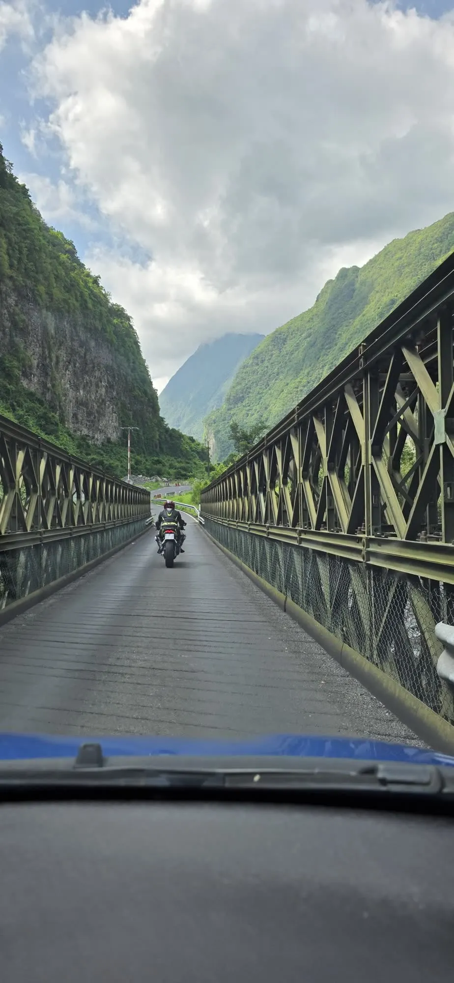 Un pont métallique étroit à poutres croisées, une moto arrivant en sens inverse
