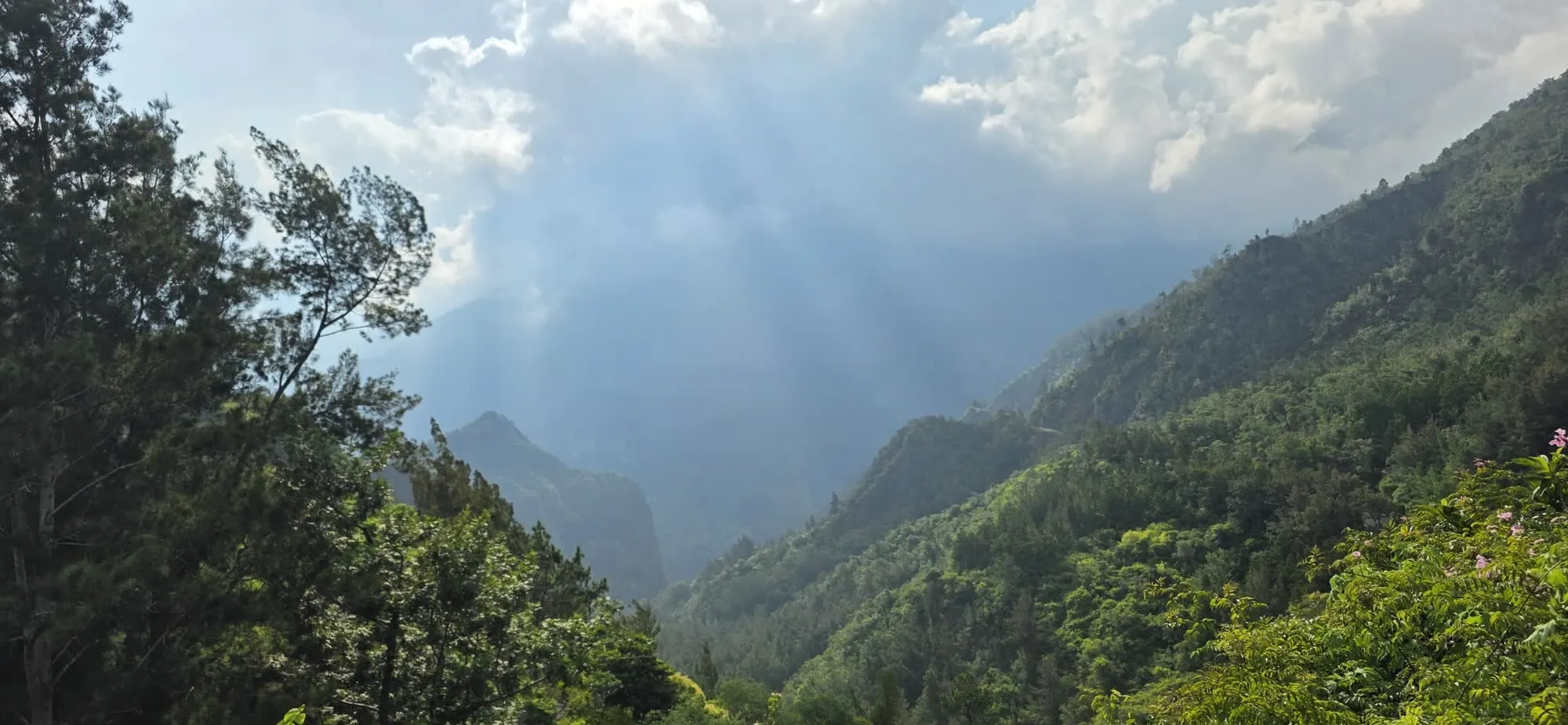 Des rais de lumière traversant les nuages au-dessus d'un cirque aux versants boisés