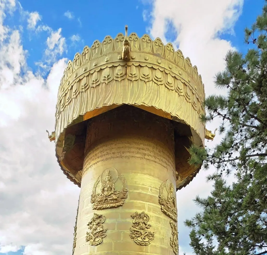 Une immense roue de prière dorée, couverte de reliefs et surmontée d'un dais sculpté