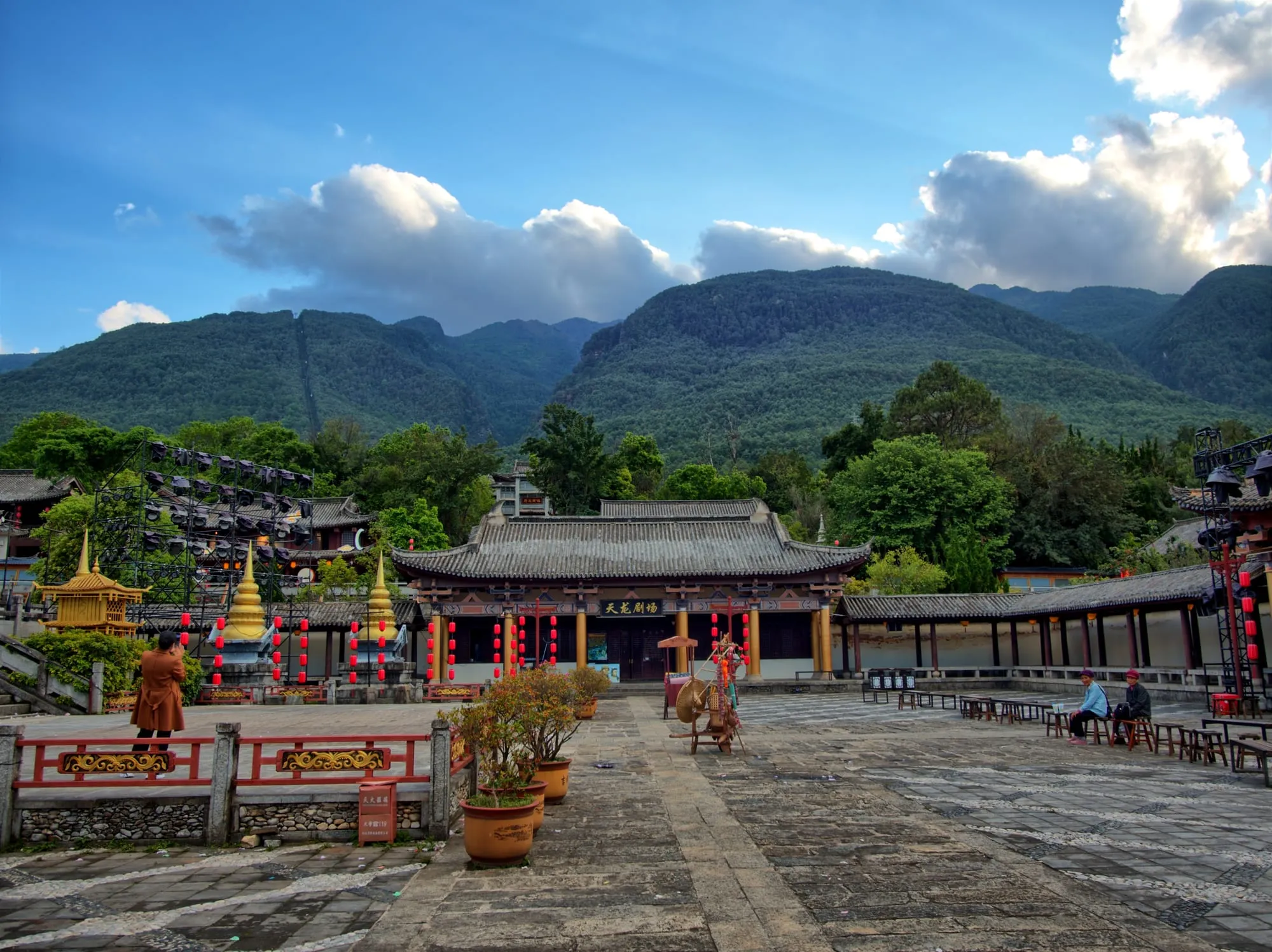 Un ensemble de temples aux toits recourbés devant une chaîne de montagnes, sous un ciel nuageux